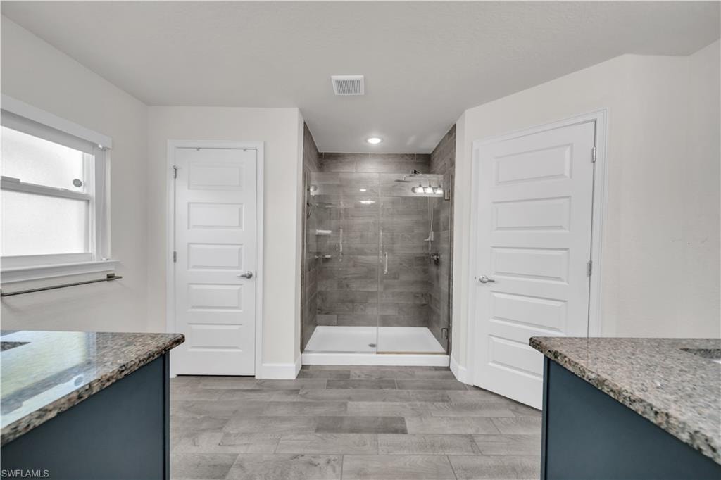 Granite countertops, wood-finish flooring, glass-enclosed shower, white five-panel doors, and recessed lighting