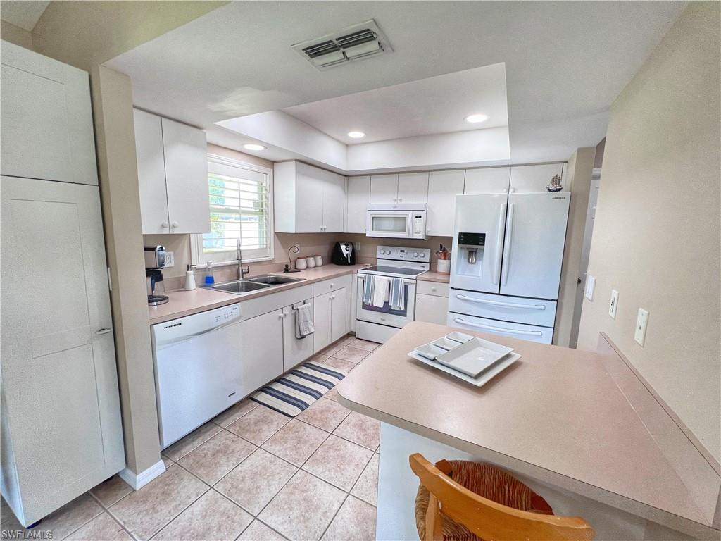 Kitchen featuring white appliances, a raised ceiling, light countertops, a breakfast bar, and recessed lighting