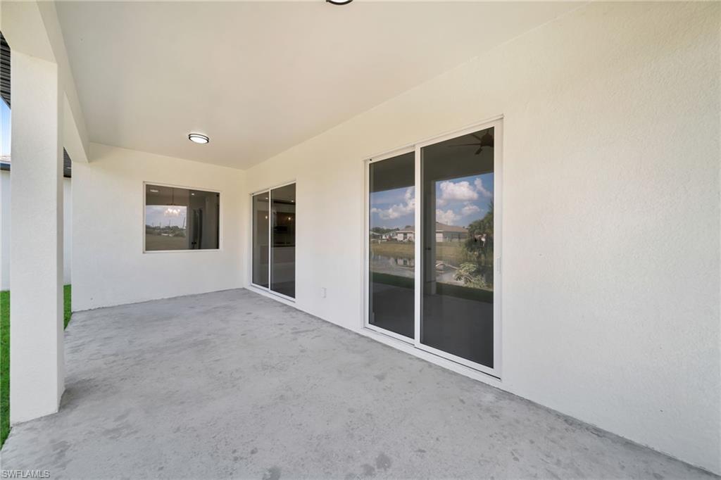 Covered lanai with concrete flooring, two ceiling-mounted light fixtures, a large window, and sliding glass doors