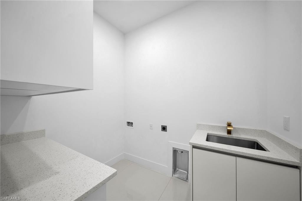 Integrated laundry space featuring white cabinetry, light-toned countertops, a stainless steel sink, and a gold-finish faucet
