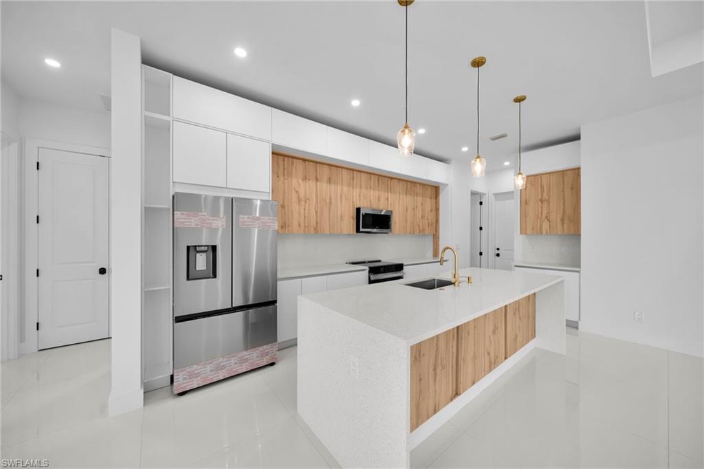 Modern kitchen featuring a large center island with integrated sink, stainless steel appliances, wood-finish cabinetry, and recessed lighting
