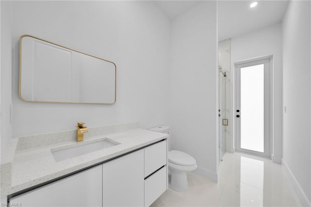 Bathroom #2: Vanity with an integrated rectangular sink and gold-finish faucet, white cabinetry, a toilet, a glass-enclosed shower with a gold-finish shower head, and an exterior access glass door