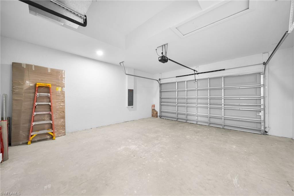 Spacious garage with an automatic overhead door, concrete flooring, and ceiling-mounted lighting