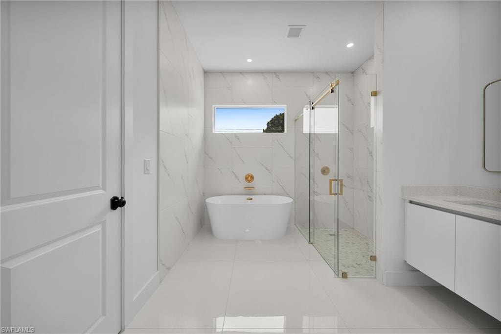 Freestanding soaking tub, walk-in shower with glass enclosure, single vanity with integrated sink, white large format floor tile, and marble-look wall tile