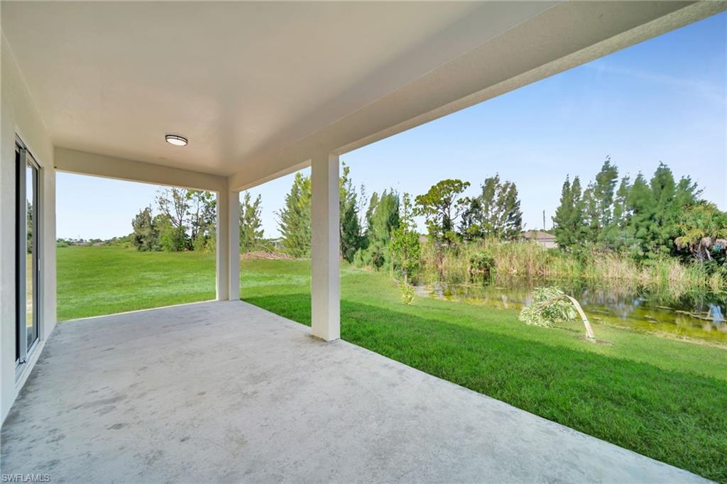 Covered concrete lanai with a flush-mount overhead light, overlooking a grassy area and a natural water feature