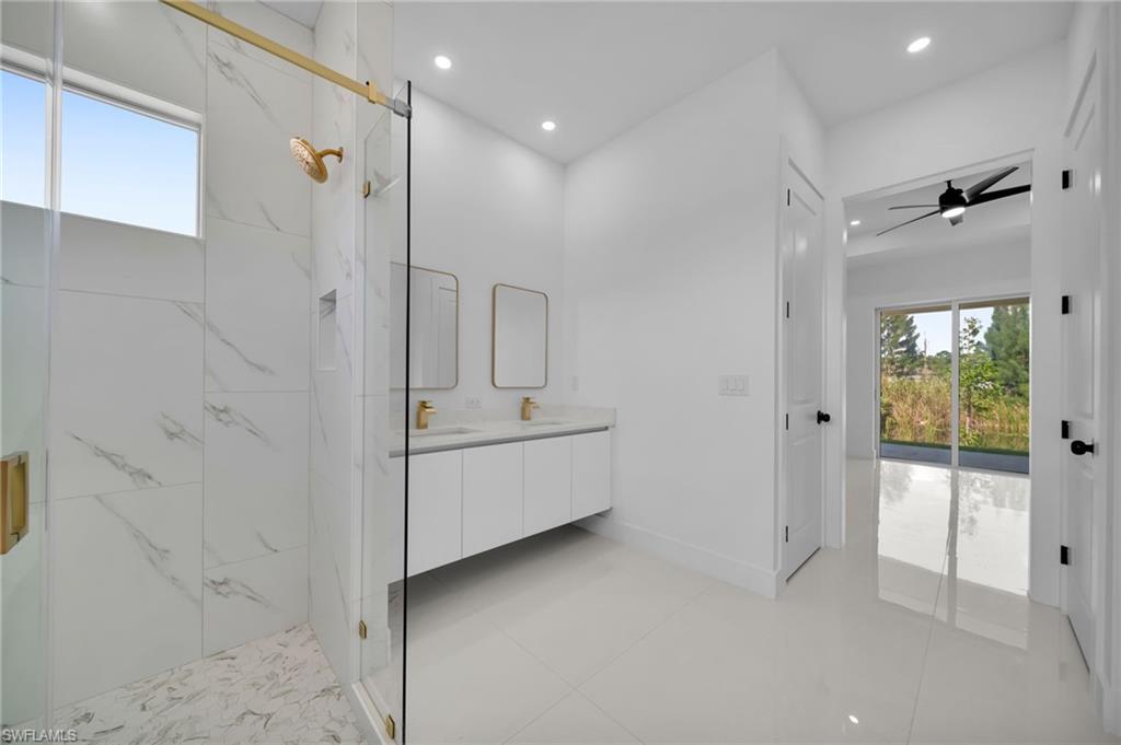 Spacious bathroom featuring a glass-enclosed shower with gold-finish fixtures, a dual vanity with rectangular mirrors, and a window for natural light