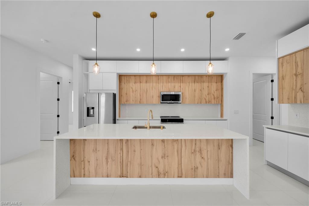 Modern kitchen featuring an expansive island with a waterfall countertop, integrated stainless steel appliances, a combination of wood-finish and white cabinetry, and pendant lighting
