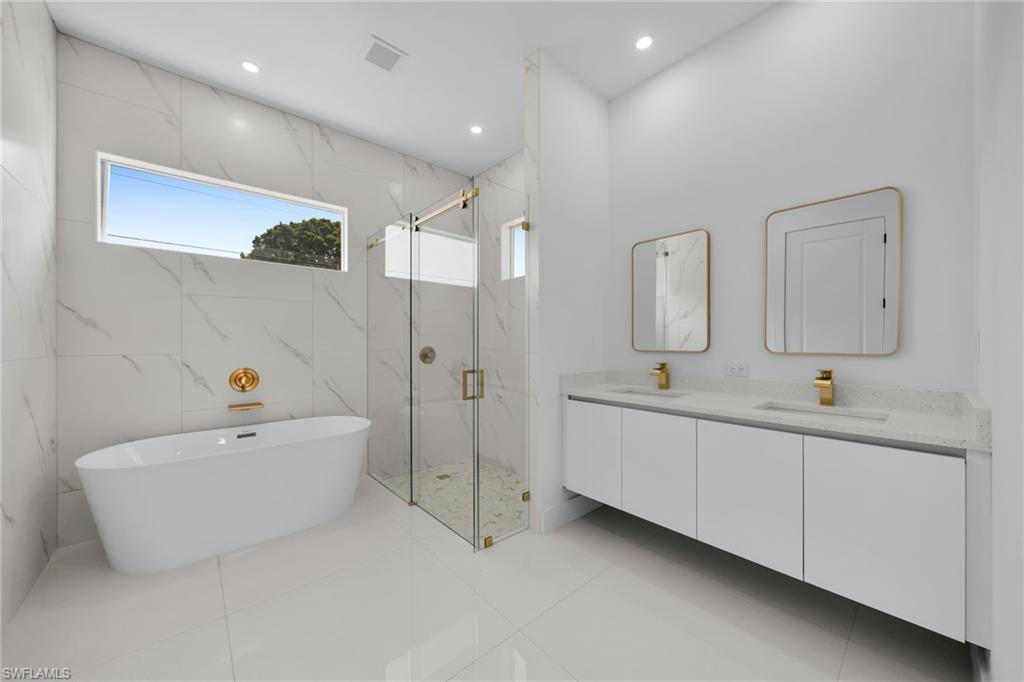 Freestanding soaking tub, glass-enclosed shower, dual floating vanities with undermount sinks, and gold-finish fixtures