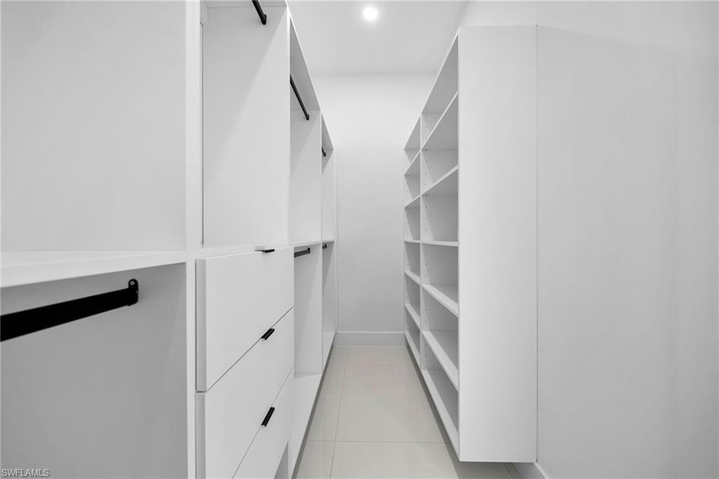 Custom walk-in closet featuring floor-to-ceiling white cabinetry with multiple shelving sections, integrated hanging rods with black hardware accents, and recessed ceiling lighting throughout the space