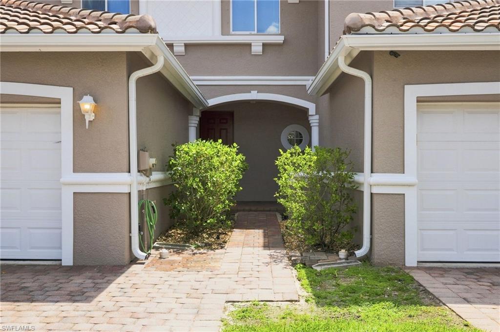 Stucco exterior with terracotta-style roof tiles, dual garage doors, arched entryway, and brick paver walkway