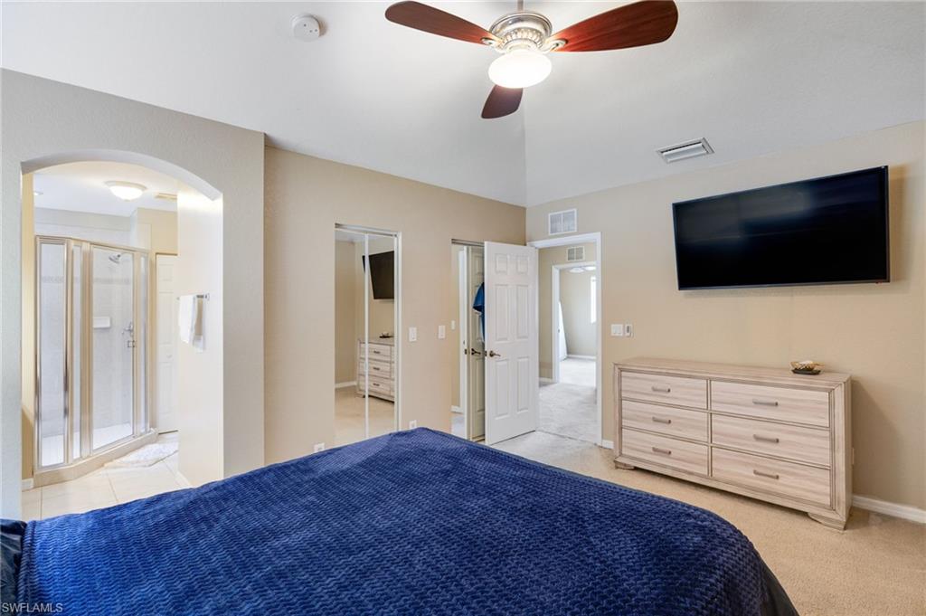 Vaulted ceiling with a ceiling fan, arched doorway, and a glass-enclosed shower with tiled walls