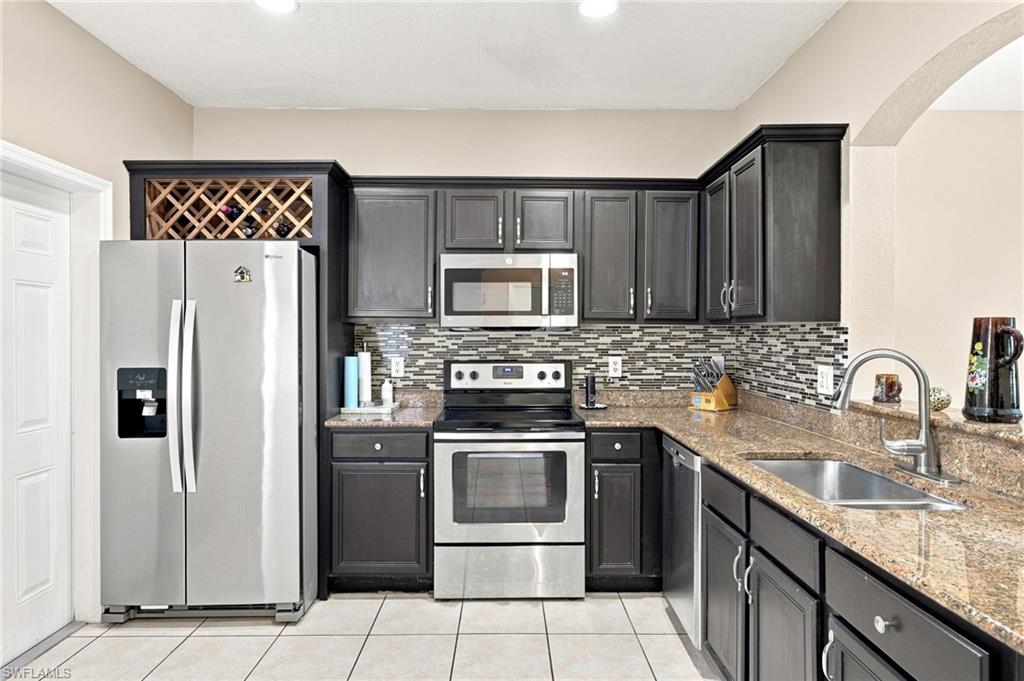 Dark-finish cabinetry, granite countertops, tile backsplash, stainless steel appliances, and a built-in wine rack