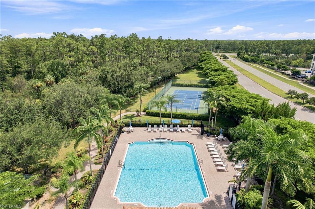 Expansive outdoor pool with a surrounding paver deck, a tennis court, and mature landscaping