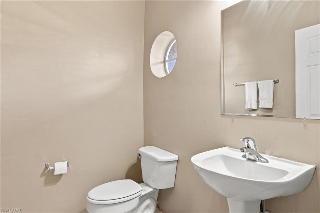 Pedestal sink with chrome faucet, wall-mounted mirror, and round accent window