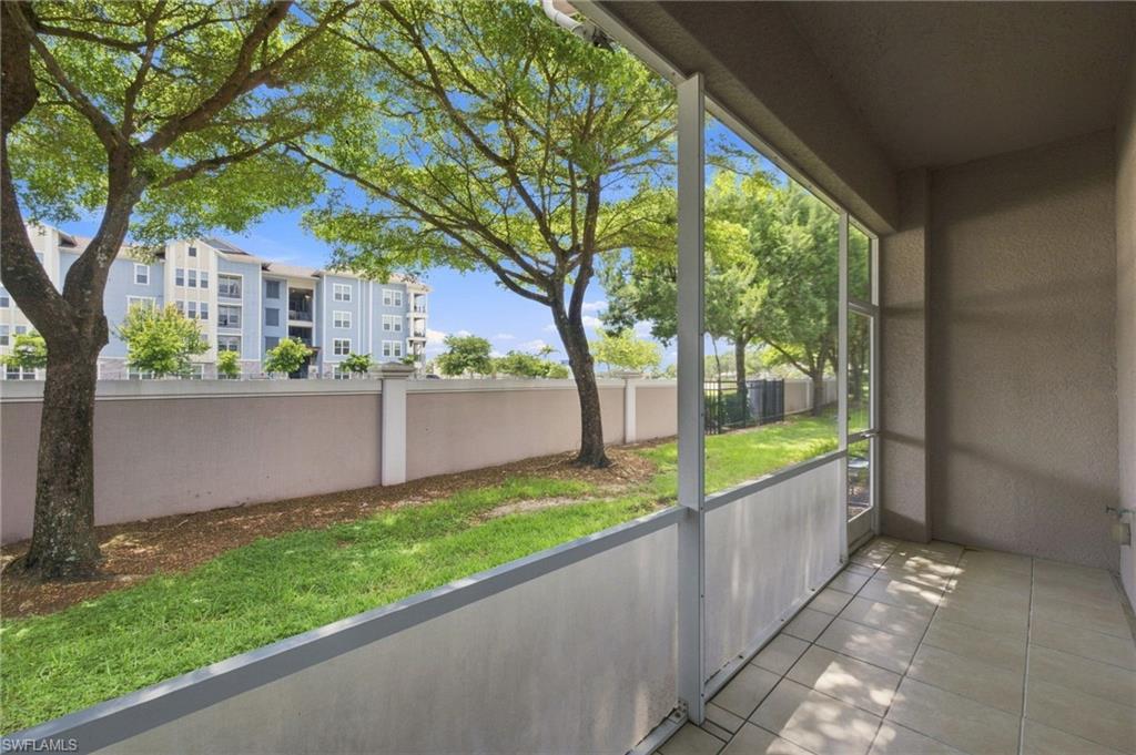 Covered patio with expansive glass sliding doors opening to a manicured lawn bordered by mature shade trees and a perimeter fence