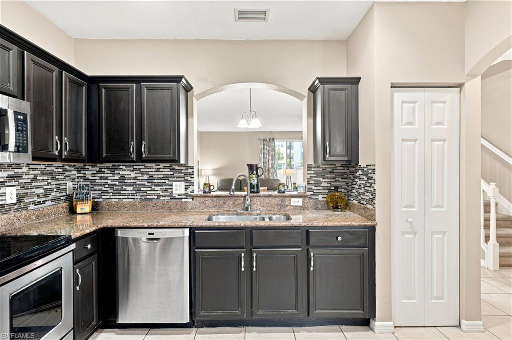 Kitchen featuring dark wood-finish cabinetry, stainless steel appliances, a tile backsplash, and stone-look countertops