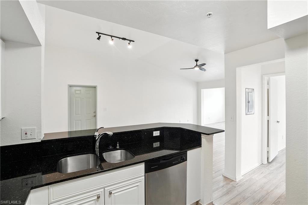 Kitchen with stainless steel dishwasher, light wood-type flooring, ceiling fan, dark stone countertops, and vaulted ceiling