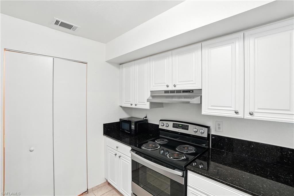 Kitchen featuring under cabinet range hood, electric range, dark stone counters, white cabinetry, and light tile patterned flooring