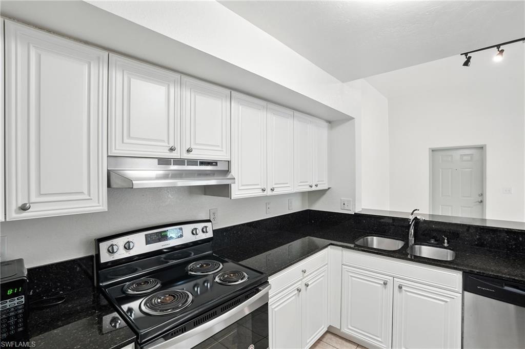Kitchen featuring stainless steel appliances, under cabinet range hood, white cabinetry, dark stone counters, and light tile patterned floors