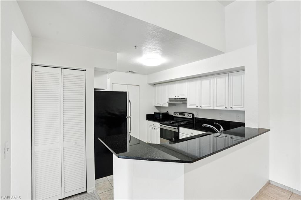 Kitchen with stainless steel range with electric stovetop, freestanding refrigerator, light tile patterned flooring, under cabinet range hood, and a peninsula
