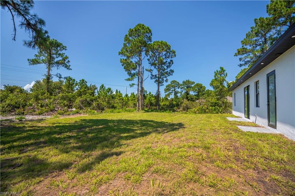Expansive grounds featuring a manicured lawn bordered by mature pine and hardwood trees, with a modern white residence offering multiple glass sliding doors and direct outdoor access