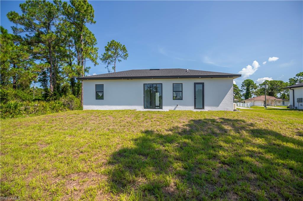 Rear exterior featuring a white stucco finish, dark-framed windows, and a glass-paneled entry door