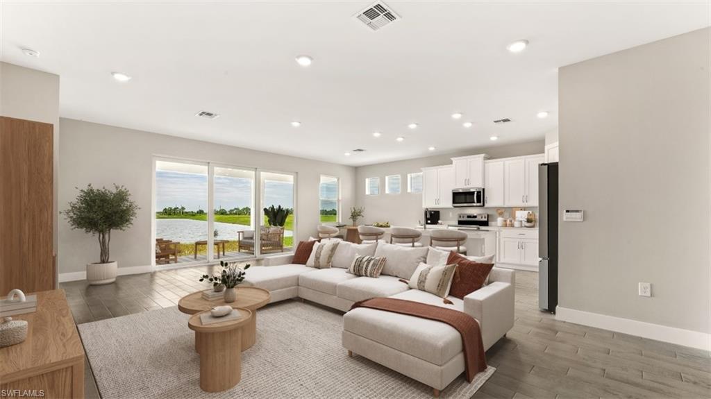 Open concept living space with recessed lighting, wood-finish flooring, and white kitchen cabinetry