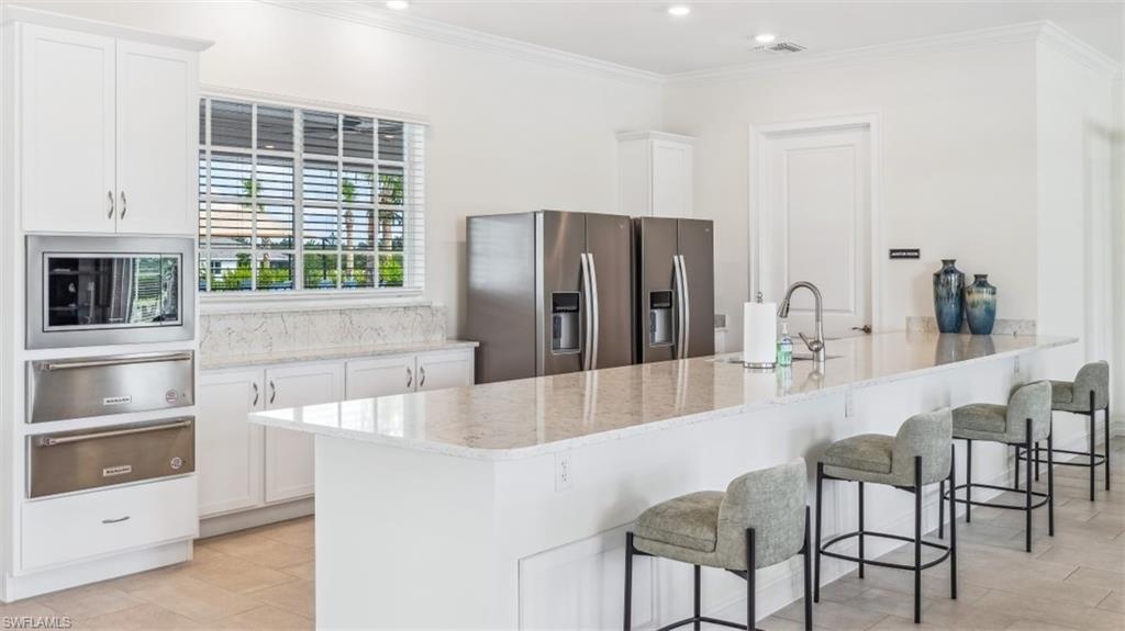 White cabinetry, light-toned flooring, stainless steel appliances, and a large kitchen island with a built-in sink