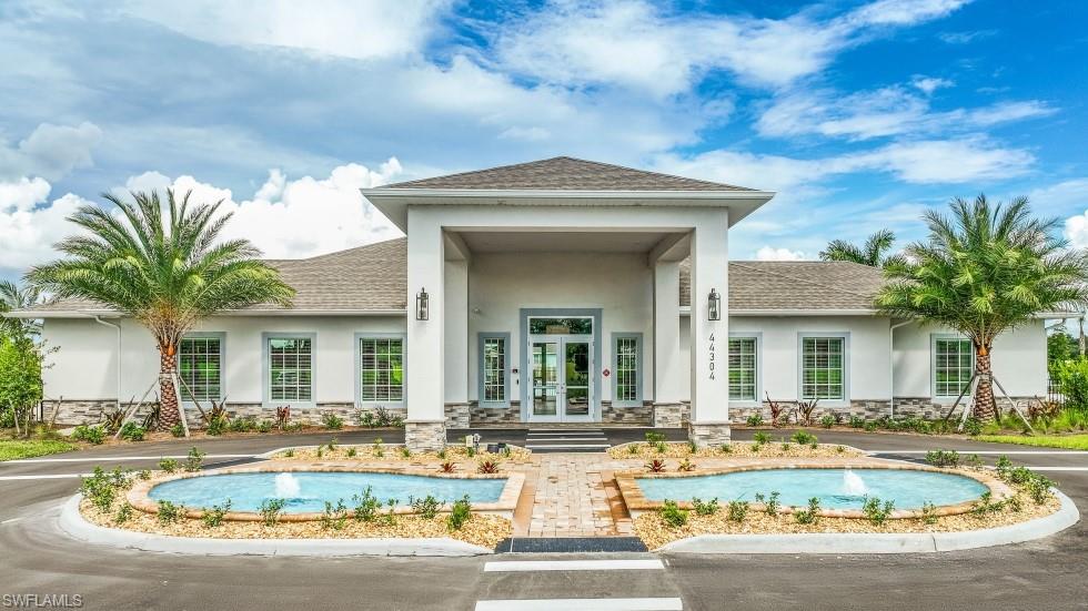 Stucco exterior with stone accenting, prominent portico entrance, dual water features, and mature palm trees