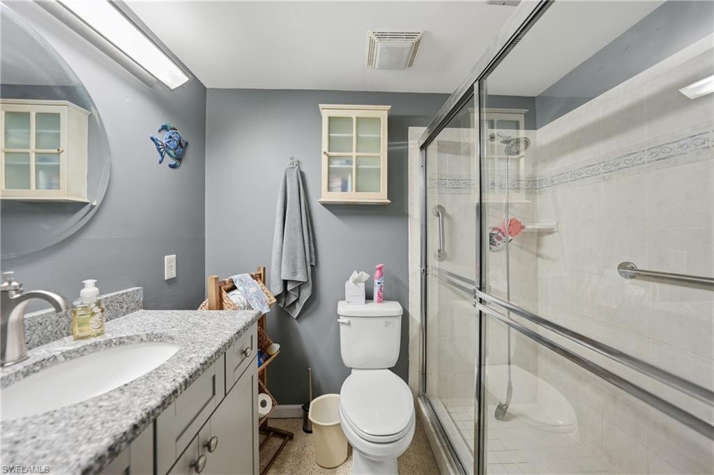 Vanity with integrated sink and speckled countertop, wood-finish cabinetry, built-in wall cabinet, framed glass shower enclosure, and tiled shower walls