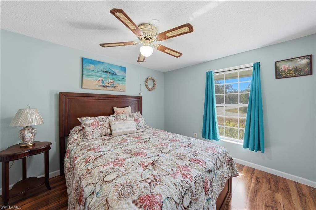 Serene second bedroom with light blue walls, wood-finish laminate flooring, and abundant natural light.