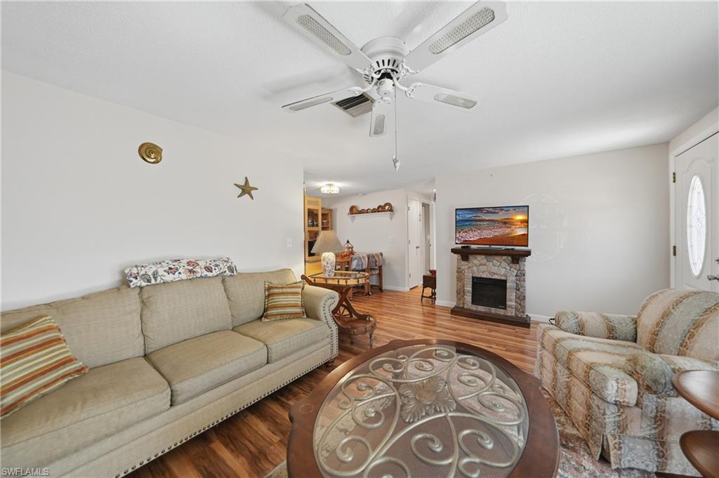 Wood-finish laminate flooring, ceiling fan, stone-clad fireplace with mantel, and a white paneled entry door with decorative glass
