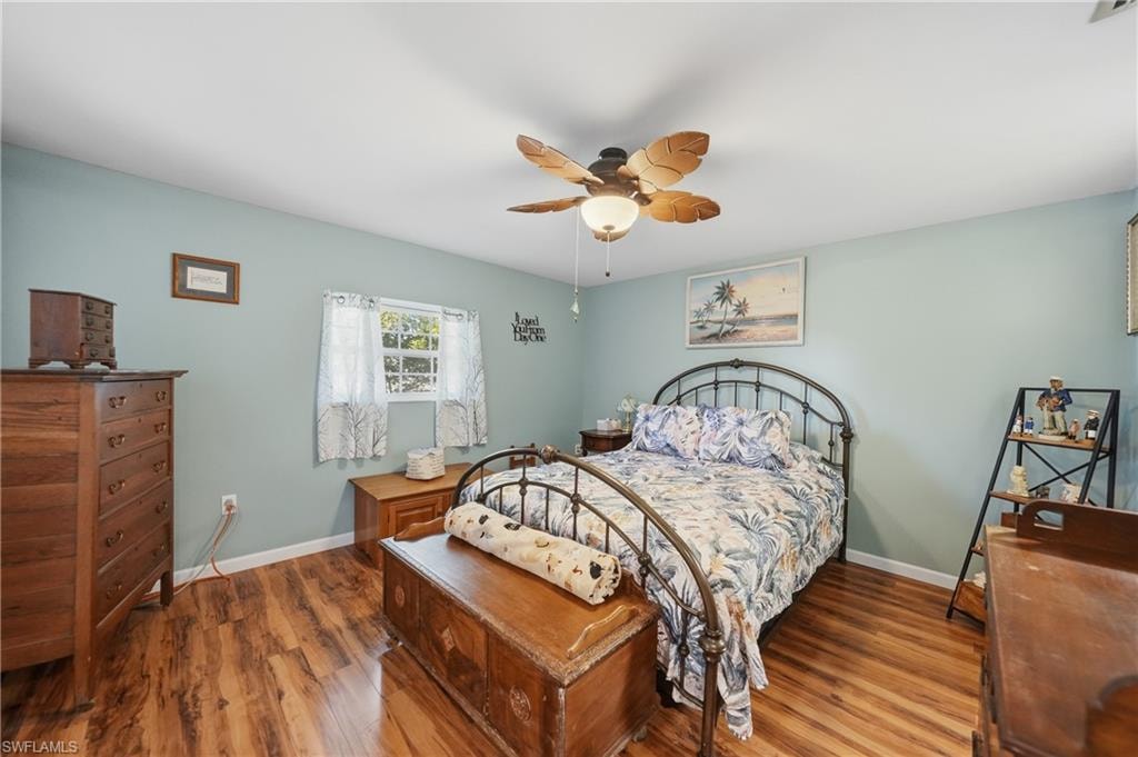 Wood-finish laminate flooring, ceiling fan with light fixture, window with natural light, light blue wall paint
