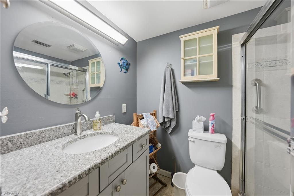 Vanity with an undermount sink and stone-finish countertop, round wall mirror, built-in wall cabinet, toilet, and glass-enclosed shower