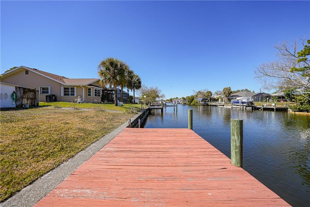 Waterfront property featuring a wooden dock, canal access, and a manicured lawn