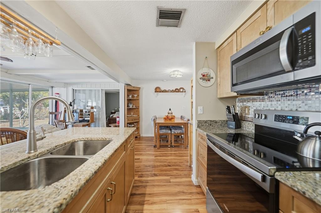 Kitchen featuring a double basin sink, stone countertops, wood-finish laminate flooring, stainless steel appliances, and wood cabinetry