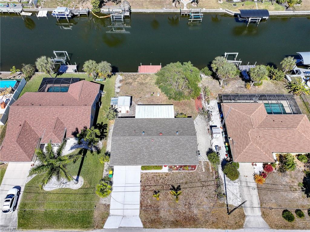 Canal-front property featuring a private dock, adjacent to homes with screened pools and mature landscaping