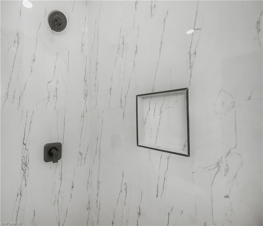 Shower with large format white tile, gray veining, black shower head, coordinating black single handle control, and a recessed shower niche with black trim