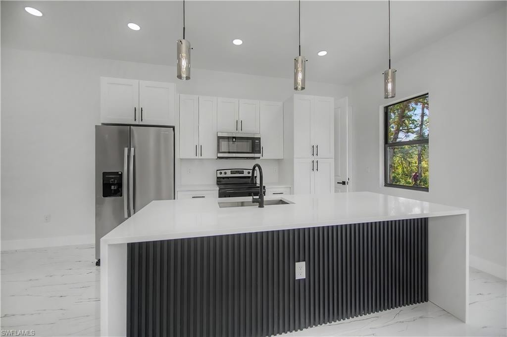 Bright kitchen featuring white cabinetry, a waterfall island with a fluted panel base, stainless steel appliances, and pendant lighting