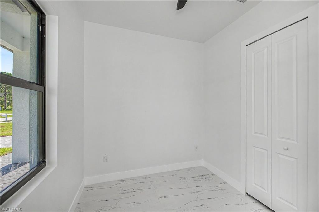 White wall finishes, white floor tile with dark veining, black-framed window, and white bi-fold closet doors