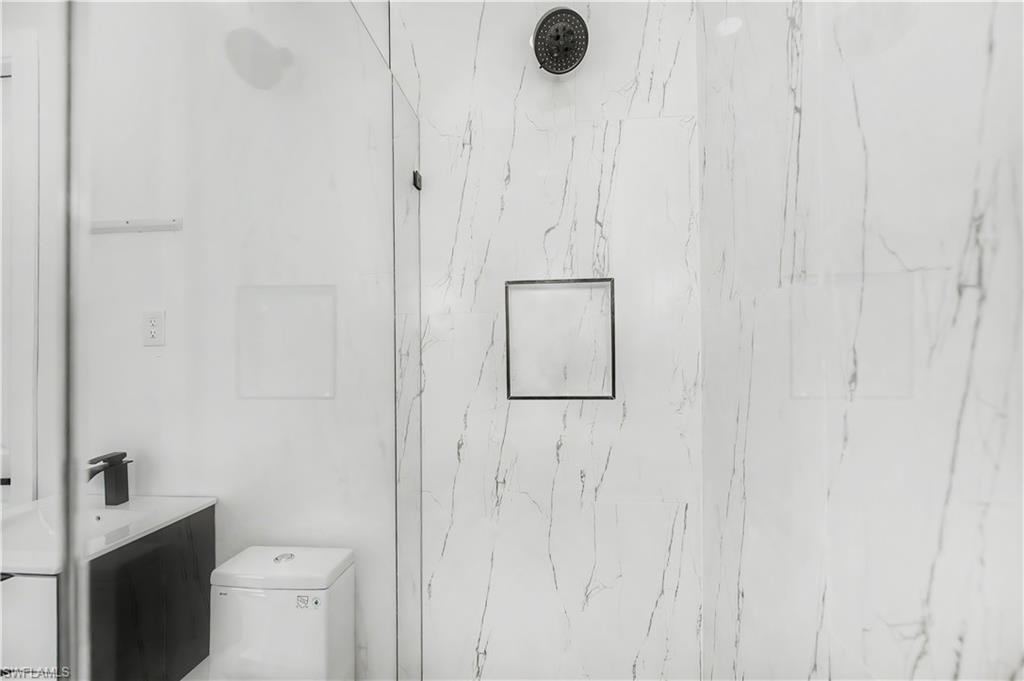 Shower enclosure featuring a black shower head, white tiled walls with subtle veining, and a built-in shower niche with a dark frame