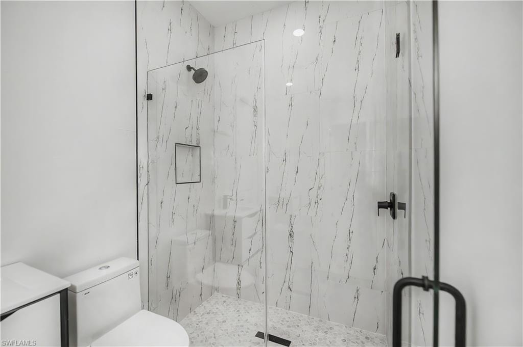 Glass-enclosed shower with white marble-style wall tiling, dark-finish rain shower head, and recessed shower niche