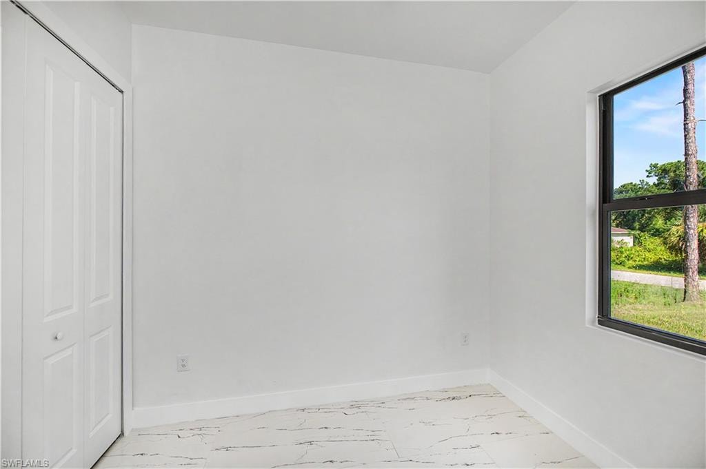 Bright, light-filled bedroom with large window framing outdoor scenery, white six-panel closet door, and light wood-finish flooring throughout
