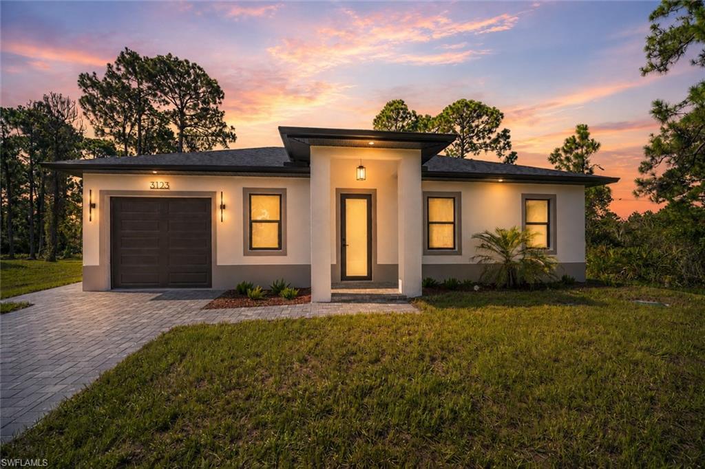 Modern exterior with a contrasting dark roof, paver driveway, and an illuminated entryway