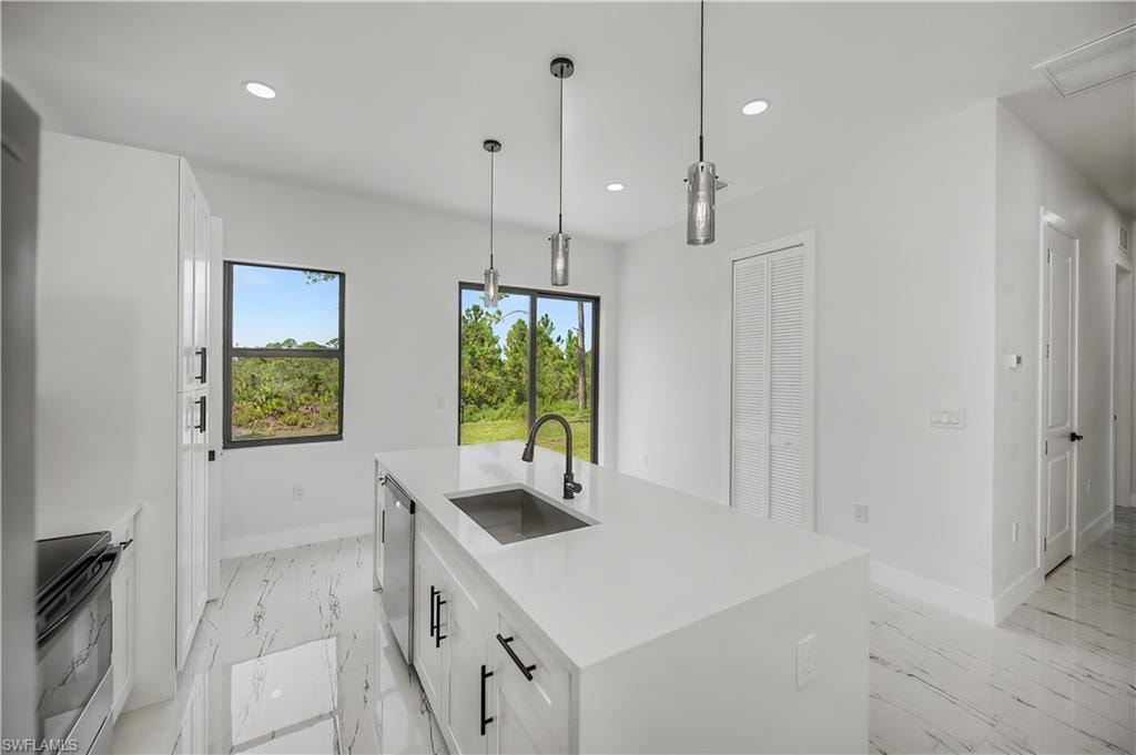 Modern kitchen featuring a central island with an undermount sink, pendant lighting, white cabinetry with black hardware, and large format tile flooring