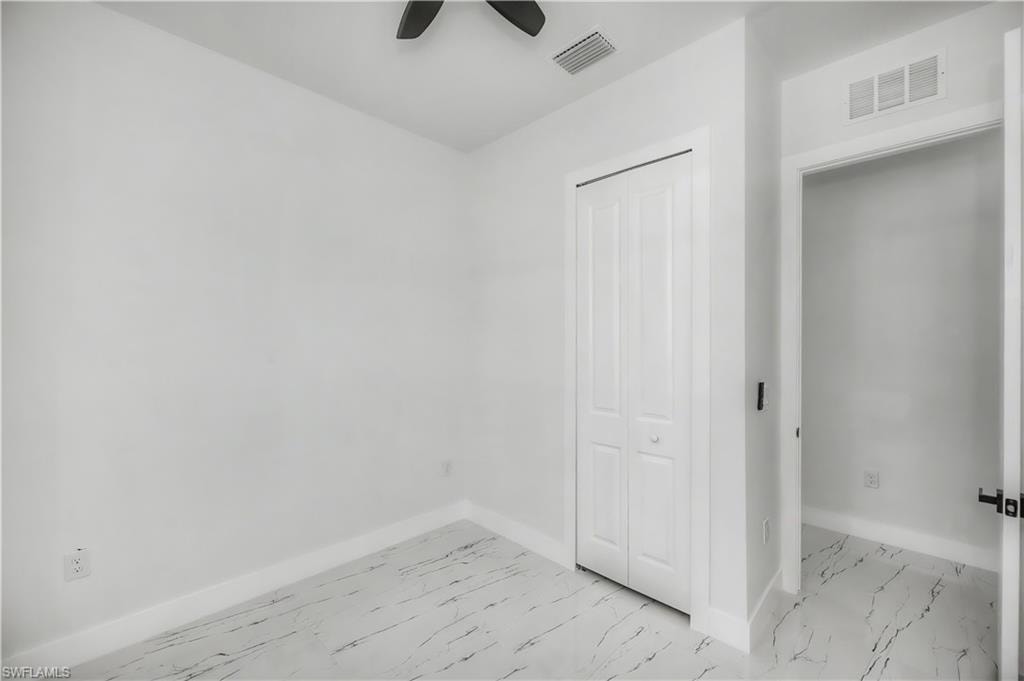 White walls with crisp white trim, marble-look flooring, white bi-fold closet doors, and black ceiling fan