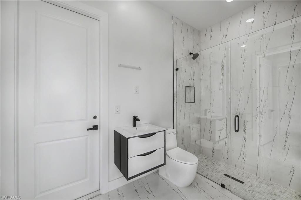 Contemporary bathroom featuring a floating vanity with integrated sink, walk-in shower with clear glass enclosure, and white tile flooring