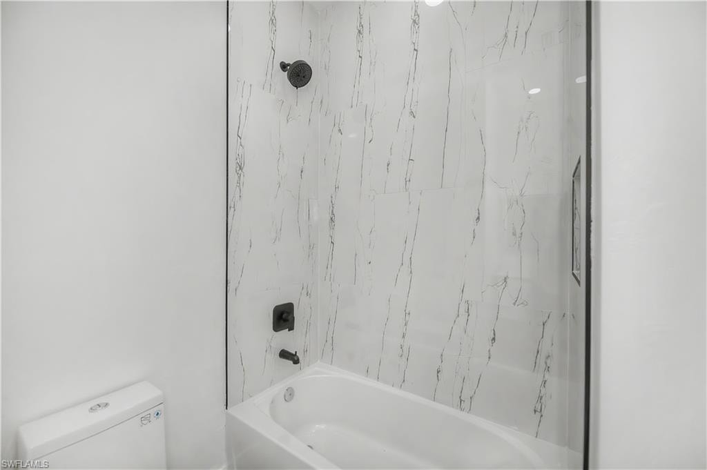 Bathtub with a shower, marble-finish wall tiling, and matte black fixtures