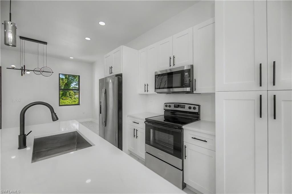 Modern kitchen featuring a large island with an undermount sink and matte black faucet, stainless steel appliances, white cabinetry with black hardware, and recessed lighting