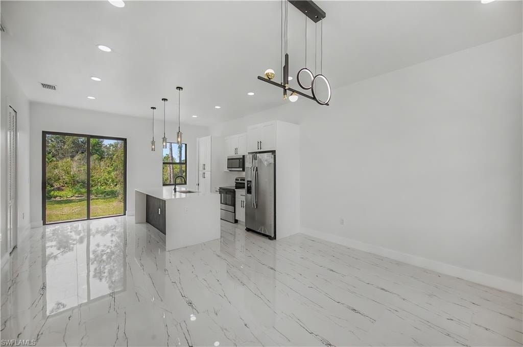 Modern kitchen featuring polished stone-finish flooring, stainless steel appliances, white cabinetry with waterfall-edge countertops, large sliding glass doors with natural light, and contemporary pendant lighting suspended from vaulted ceilings with recessed lighting throughout